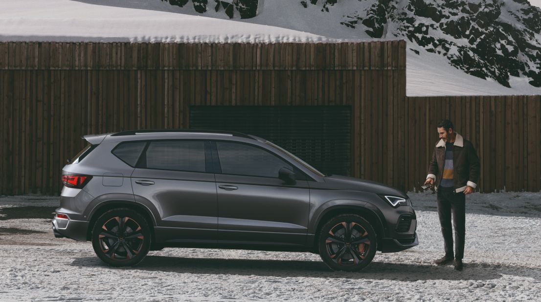 Seitenprofil eines CUPRA Fahrzeugs auf einer verschneiten Straße, während ein Mann davor steht und die Motorhaube betrachtet.