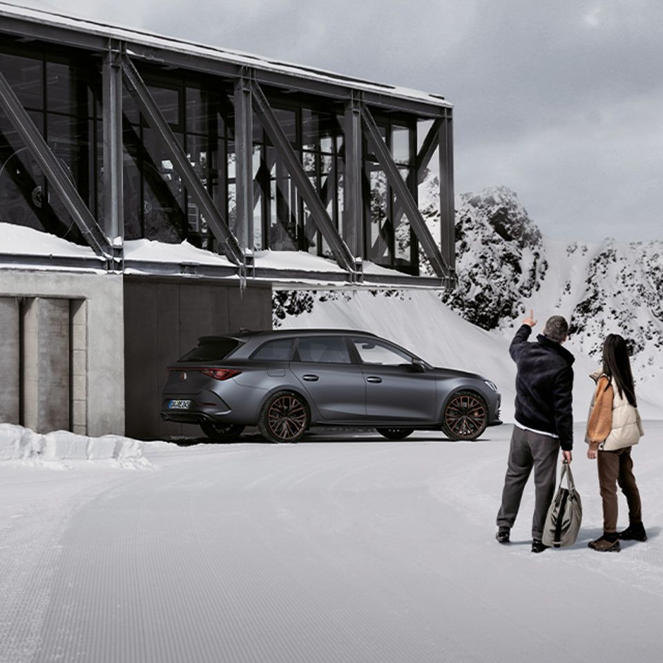 CUPRA Auto im Hintergrund, umgeben von Schnee, während zwei Personen in Winterkleidung davor stehen und die winterliche Landschaft genießen.